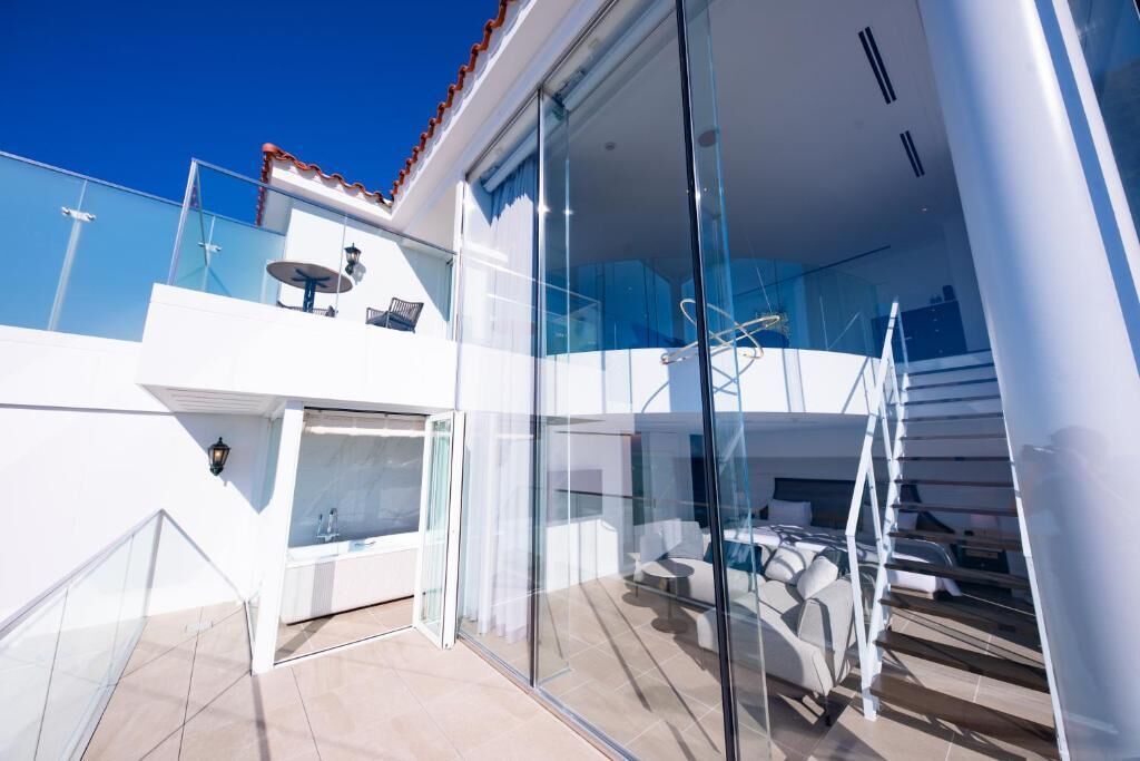 A modern, multi-level balcony with glass railings, a seating area, and a staircase.