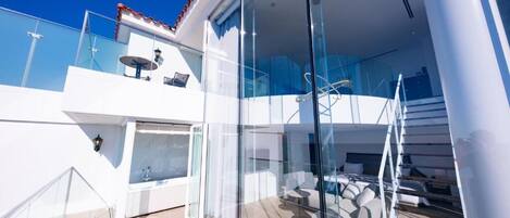 A modern, multi-level balcony with glass railings, a seating area, and a staircase.