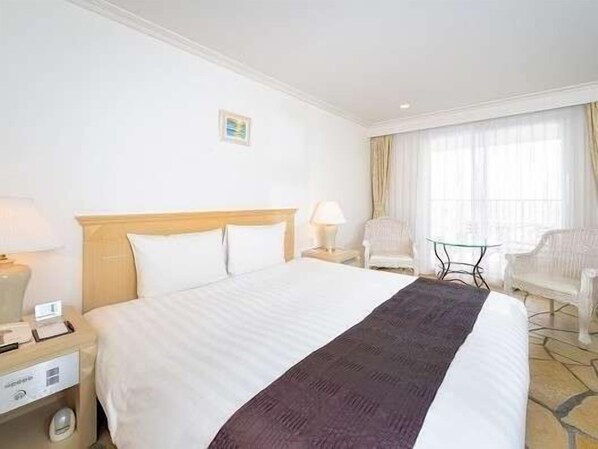 A hotel room with a large bed, two bedside tables with lamps, a small table, a chair, and a window with curtains. - Hayama Hotel Otowa NO Mori (Yokosuka)