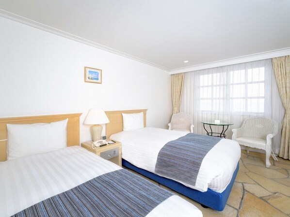 A hotel room with two beds, a small table, two chairs, a lamp, and a picture on the wall. - Hayama Hotel Otowa NO Mori (Yokosuka)