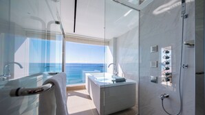 Une salle de bain moderne dotée d’une douche à parois de verre, d’une baignoire et d’une grande fenêtre donnant sur la mer.