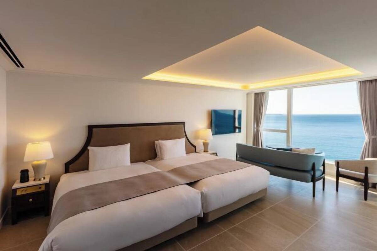 Ein Hotelzimmer mit einem großen Bett, Nachttischlampen, einem Sofa und Meerblick.