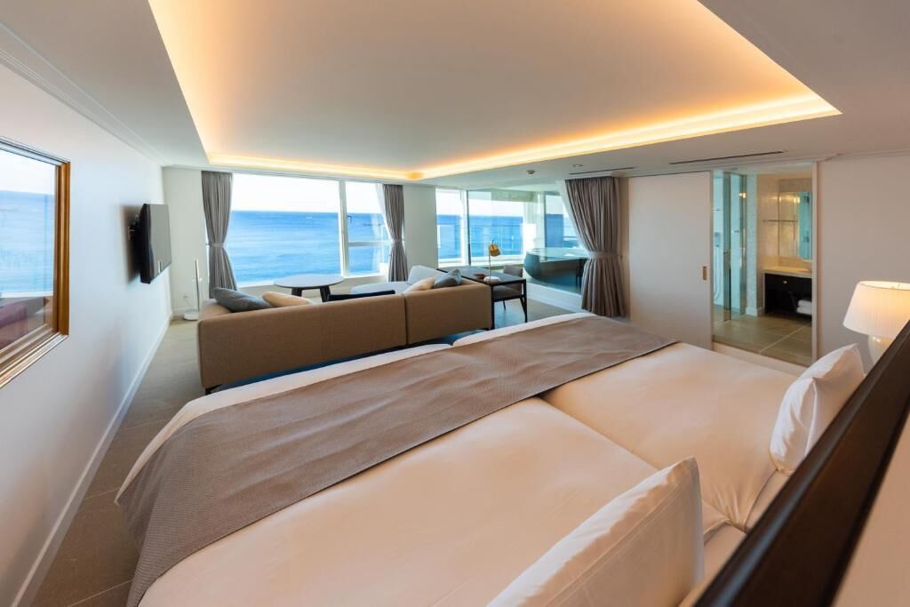 Een moderne hotelkamer met een groot bed, een bank, een eethoek en uitzicht op zee.