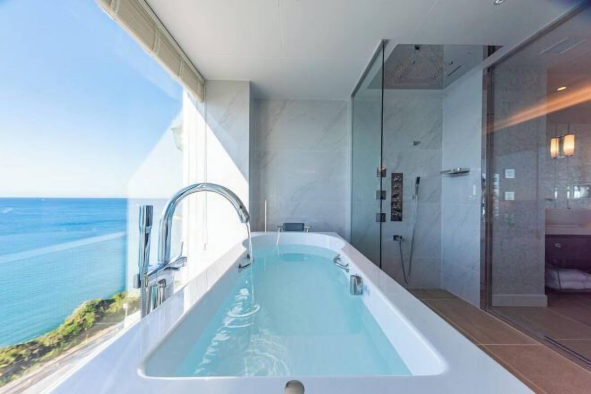 Ein modernes Badezimmer mit Badewanne, Dusche und Glastüren, mit Blick auf ein Gewässer.