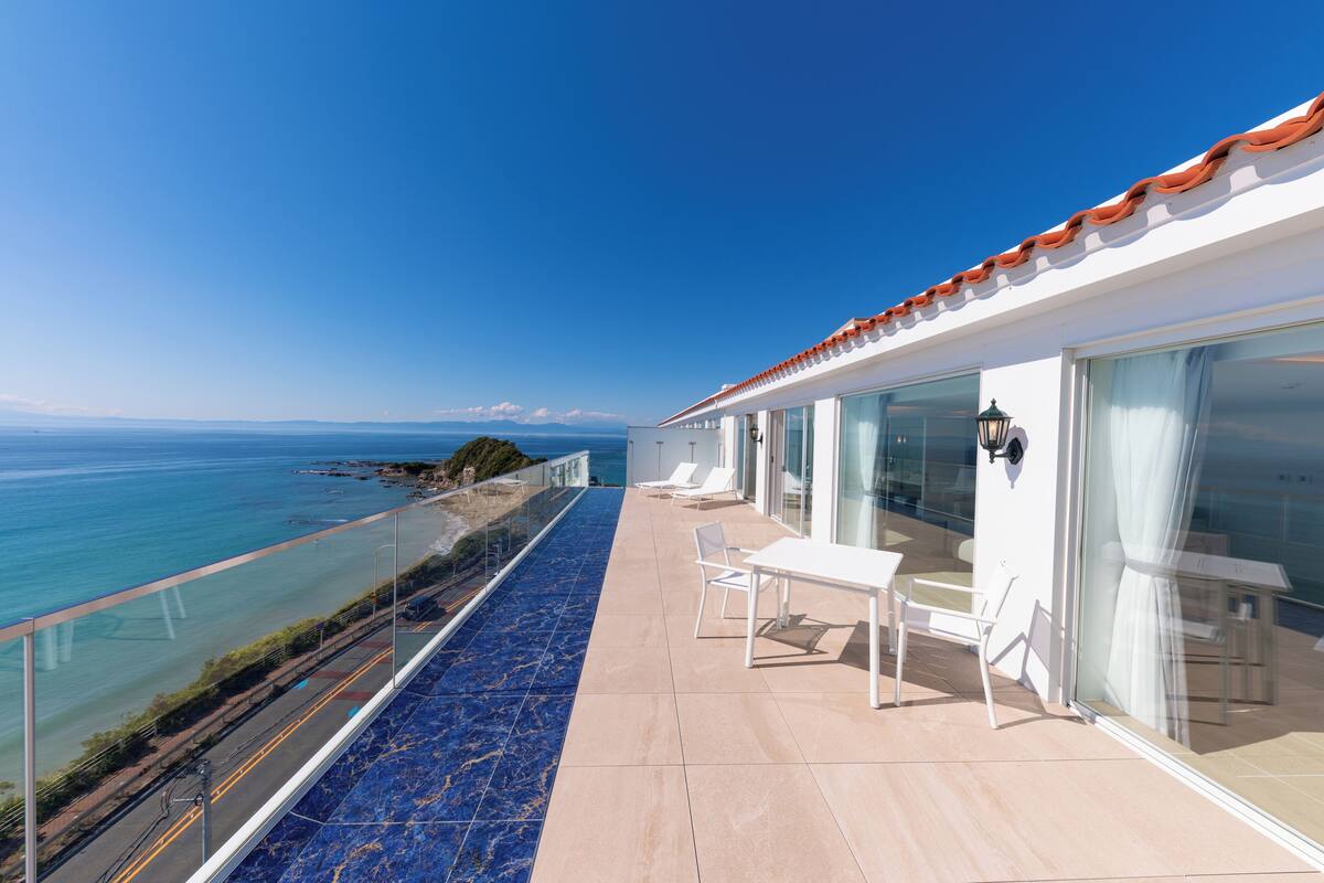 Ein Balkon mit Meerblick, einer Glasreling und einem Tisch mit Stühlen.