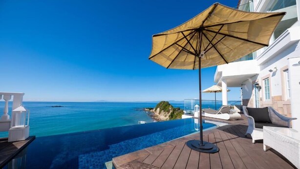 Une piscine privée offrant une vue dégagée sur la mer, une terrasse en bois et un espace détente agrémenté d’un auvent.