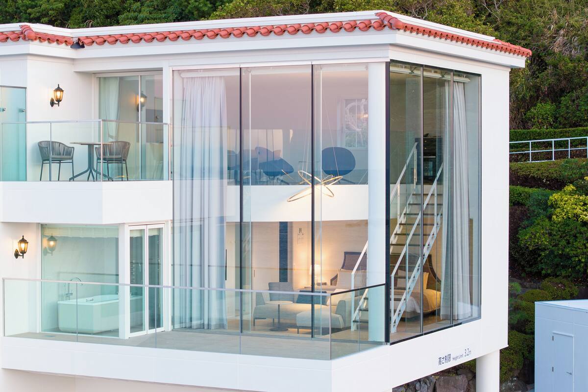 Ein modernes, zweistöckiges Gebäude mit Glasfassade, einem Balkon mit Stühlen und einer Treppe, die zum oberen Stock führt.