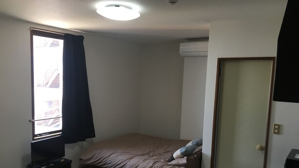 A small, compact room with a single bed, a small table, a television, and a window with curtains. - Stay inn Blue (Goto)