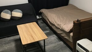A small, sparsely furnished room with a bed, a small table, a couch, and a heater. - Stay inn Blue (Goto)