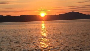A sunset over a calm body of water with a silhouette of a mountain range in the distance.
