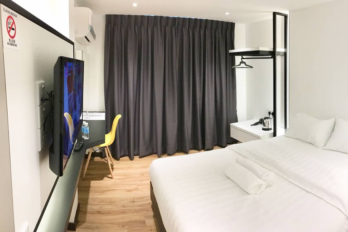 A hotel room with a bed, a desk with a computer, a chair, a curtain, and a shower area.