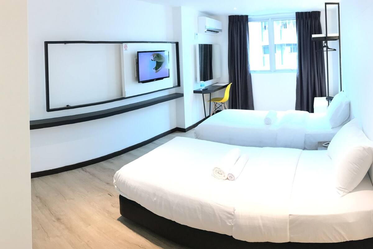 A hotel room with a shower, toilet, bed, TV, and a desk with a chair.