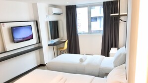 A hotel room with two beds, a desk, a TV, and a window with curtains.