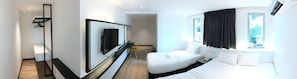 A modern hotel room with a large mirror, a white sofa, a bedside table with a phone, and a window with curtains. - Texas Inn (Sibu)