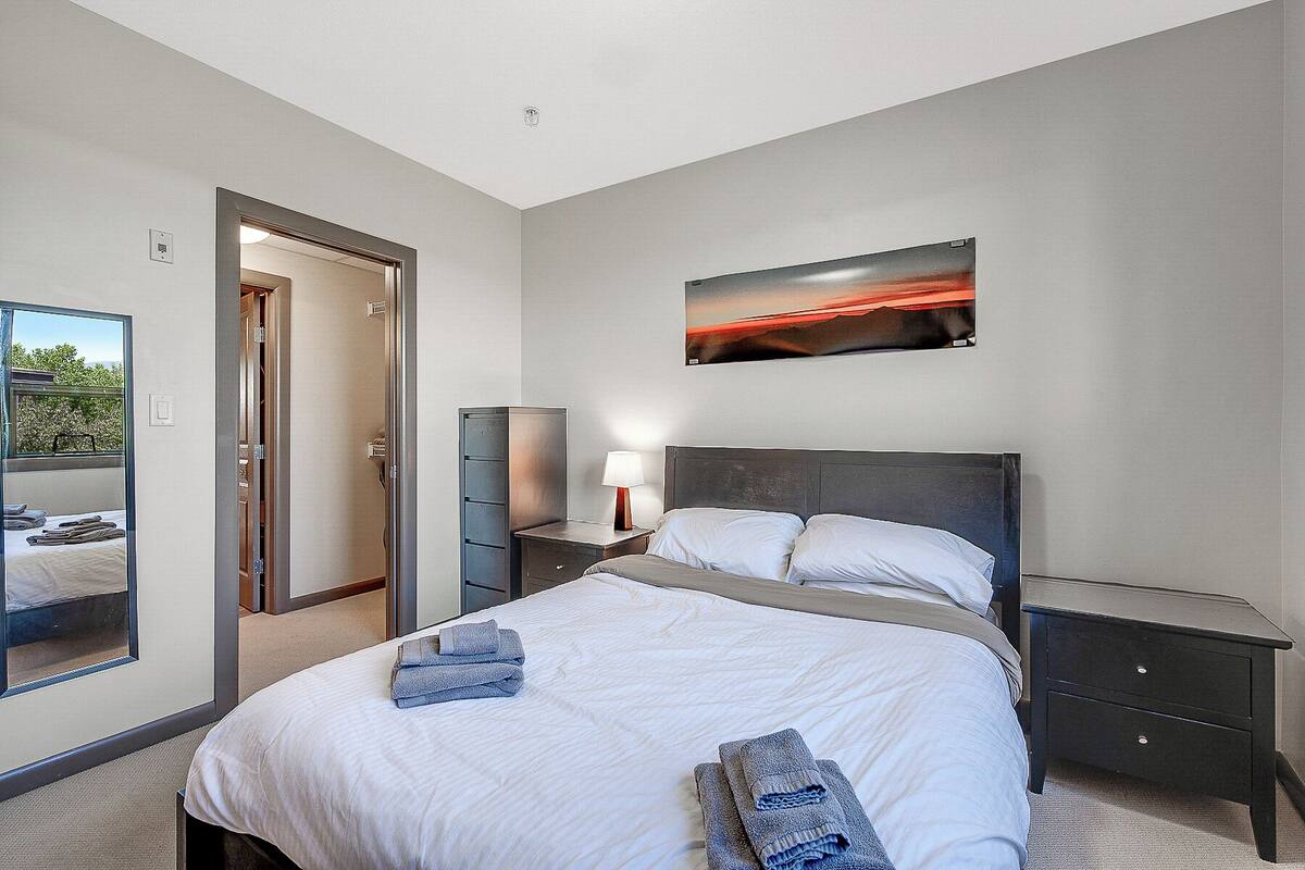 A hotel room with a bed, a nightstand, a lamp, a mirror, a wardrobe, and a painting on the wall.