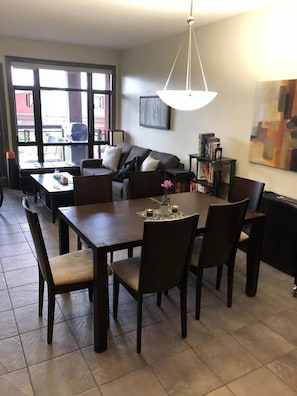 A dining area with a table and chairs, a sofa, a bookshelf, and a large window. - Playa Del Sol Retreat 550 | Pool + Hot Tub | Sleeps 6 (Kelowna)
