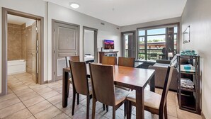 A dining area with a table and chairs, a television, and a view of the outdoors. - Playa Del Sol Retreat 550 | Pool + Hot Tub | Sleeps 6 (Kelowna)