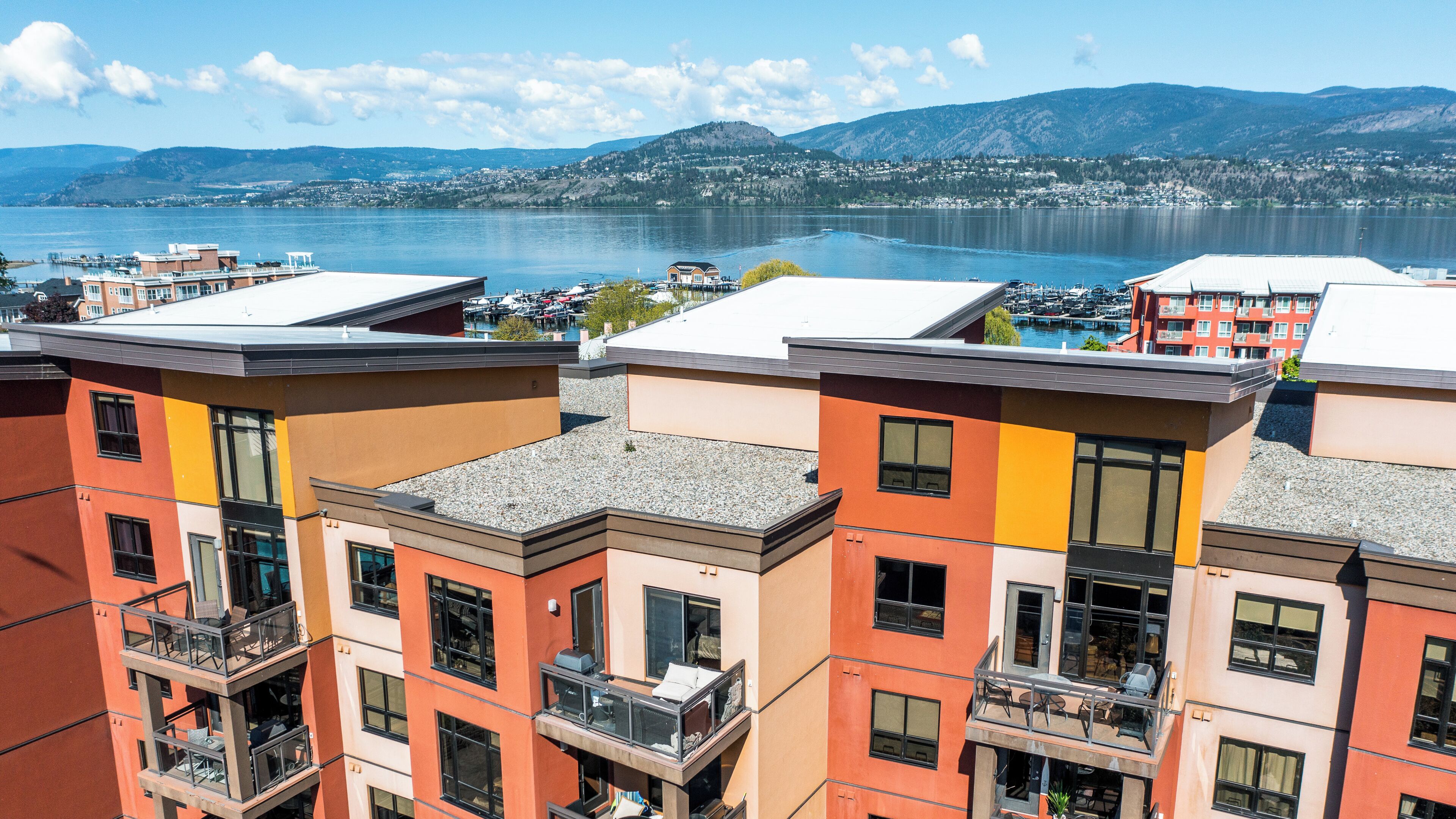 A multi-story building with balconies, a lake view, and a mountainous backdrop.