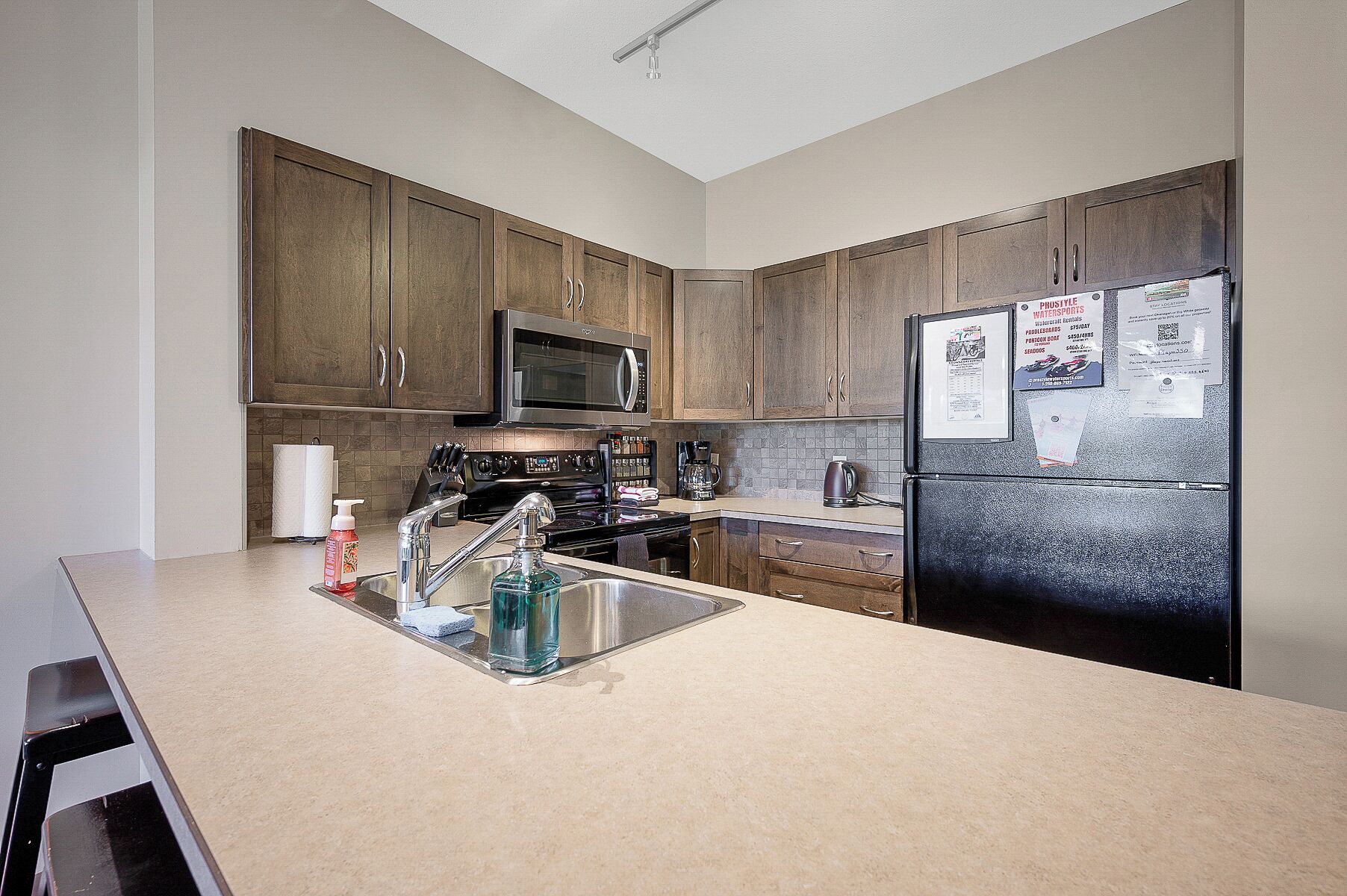 A kitchen with wooden cabinets, a stainless steel sink, a microwave, a stove, and a refrigerator.