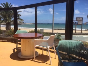 Um alpendre à beira-mar com uma mesa redonda e duas cadeiras, com vista para uma praia de areia e o oceano.