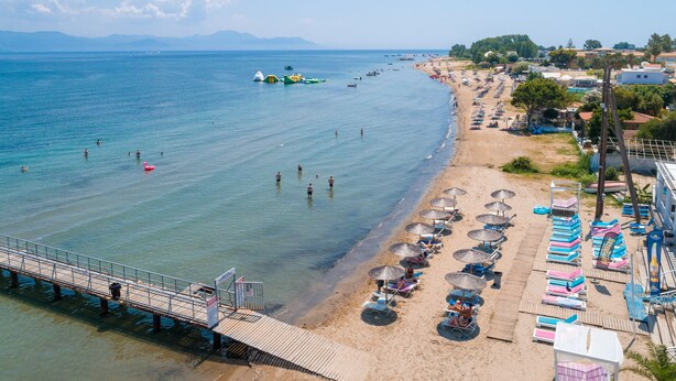 A beach with a pier, umbrellas, and beach chairs. - Paralia Studios (Corfu)