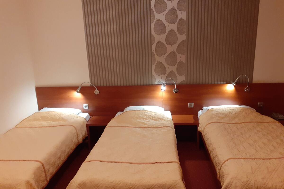 Una habitación de hotel con tres camas individuales, cada una con cabecera y lámpara de noche.