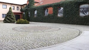 A courtyard with cobblestone paving, a large tree, and a building partially covered in ivy. - Hotel Rydzewski (Elk)