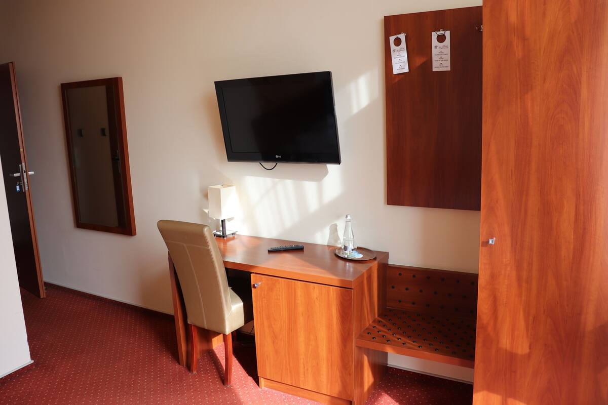 Una habitación con escritorio de madera, una silla, un televisor montado en la pared y un armario de madera.
