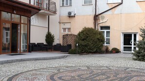 A courtyard with a mosaic floor, outdoor seating, and a building entrance. - Hotel Rydzewski (Elk)