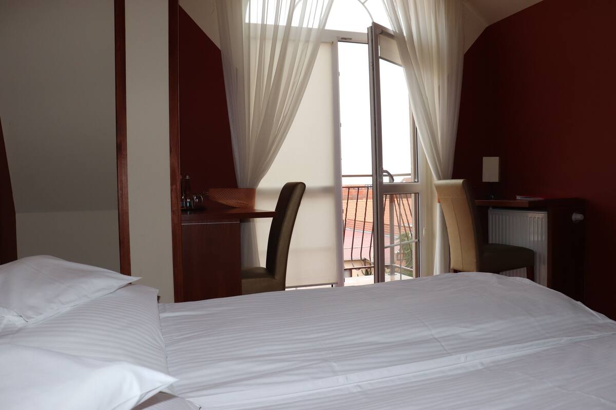 Habitación de hotel con cama, escritorio, silla y vistas al balcón exterior.
