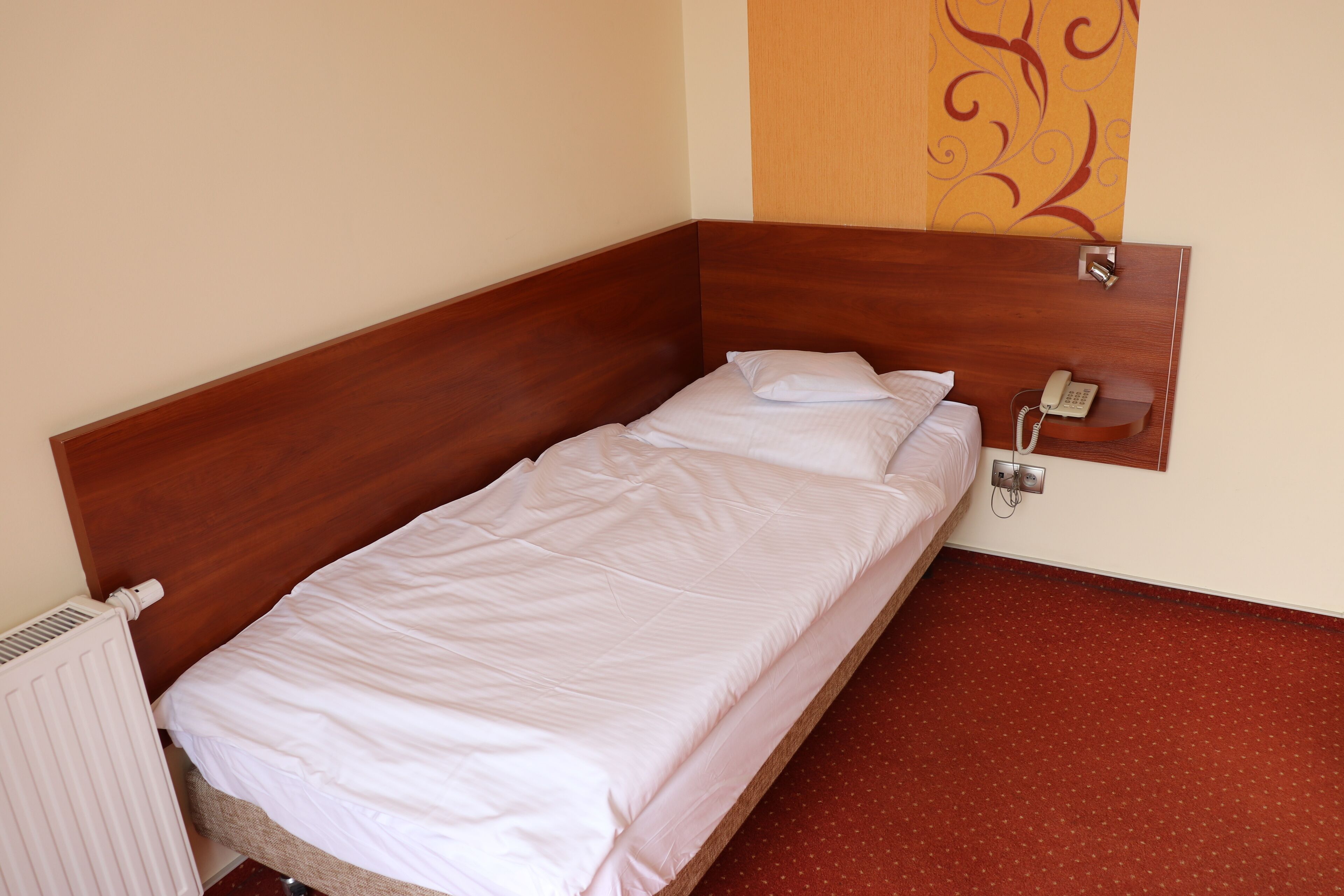 A single bed with a wooden headboard, white bedding, a telephone, and a radiator.
