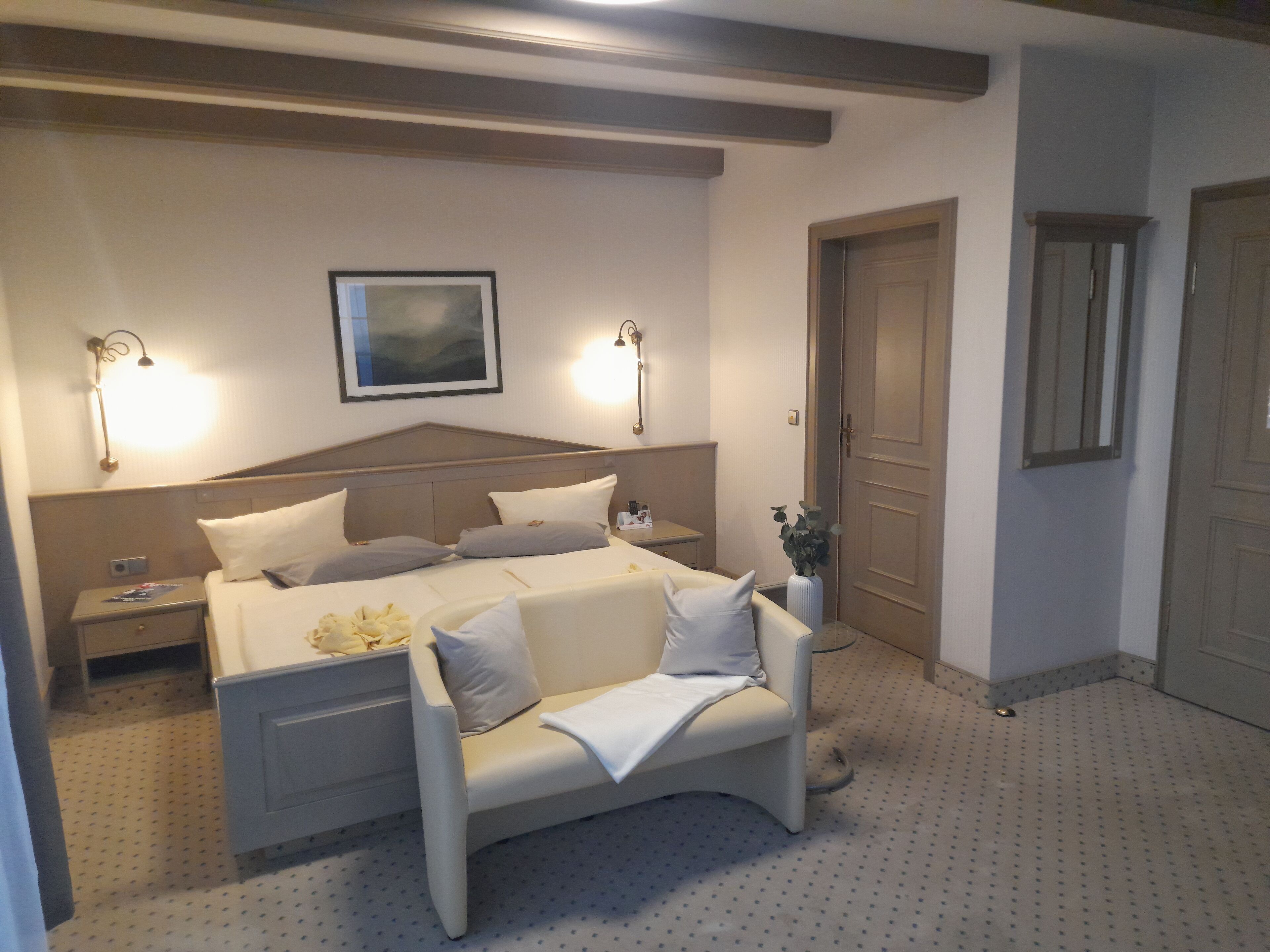 A hotel room with a bed, bedside tables, a nightstand, a lamp, a framed picture on the wall, and a door.