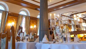 A dining area with a large, ornate ceiling fan, elegant table settings, and a chandelier.