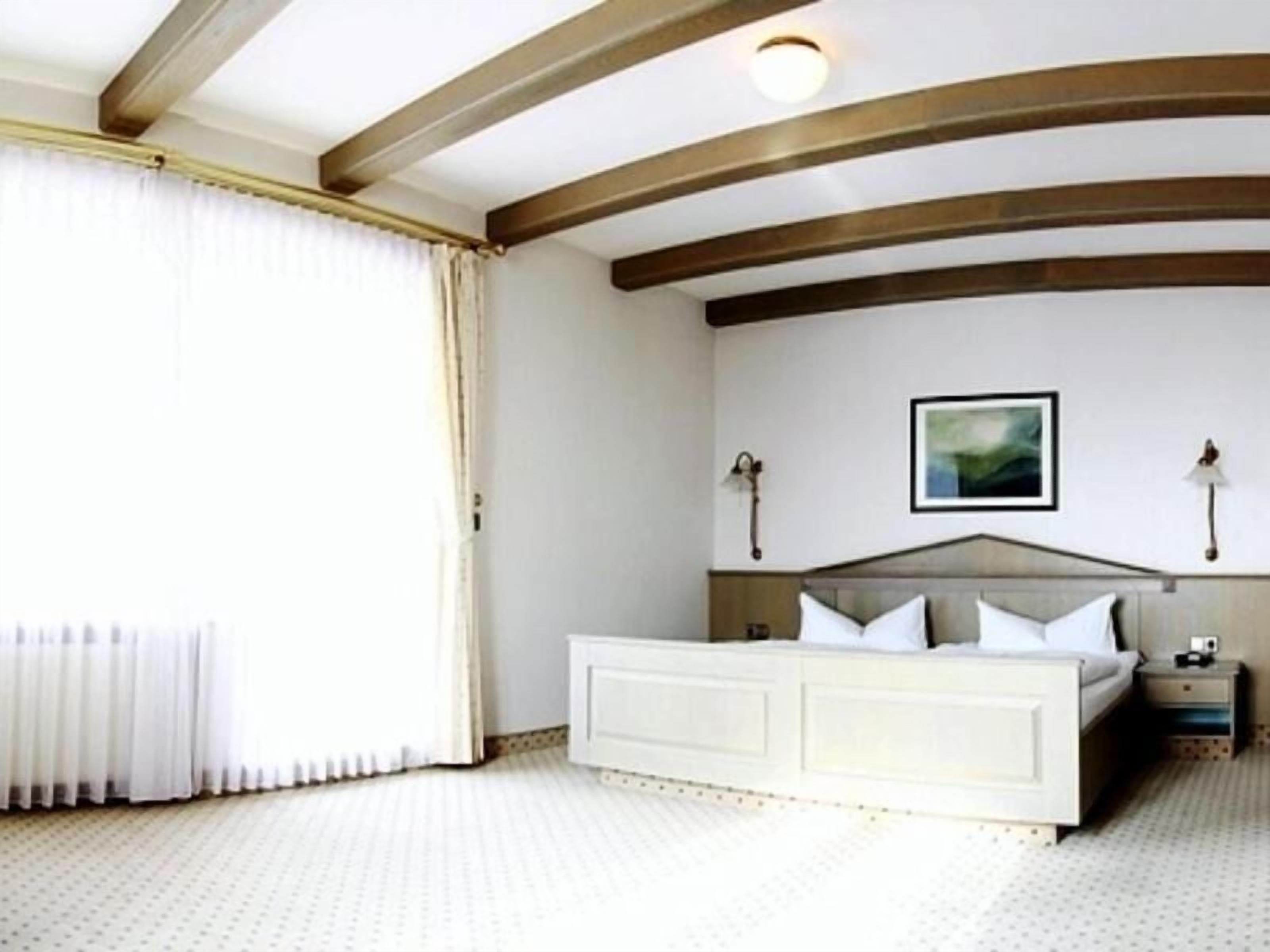 A bedroom with a large bed, a nightstand, a wall-mounted lamp, and a painting.