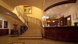 A grand staircase with ornate railings, a reception desk, and a library area.