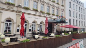 A hotel with outdoor seating, a sign for 'Hotel Drei Schwannen', and flags.
