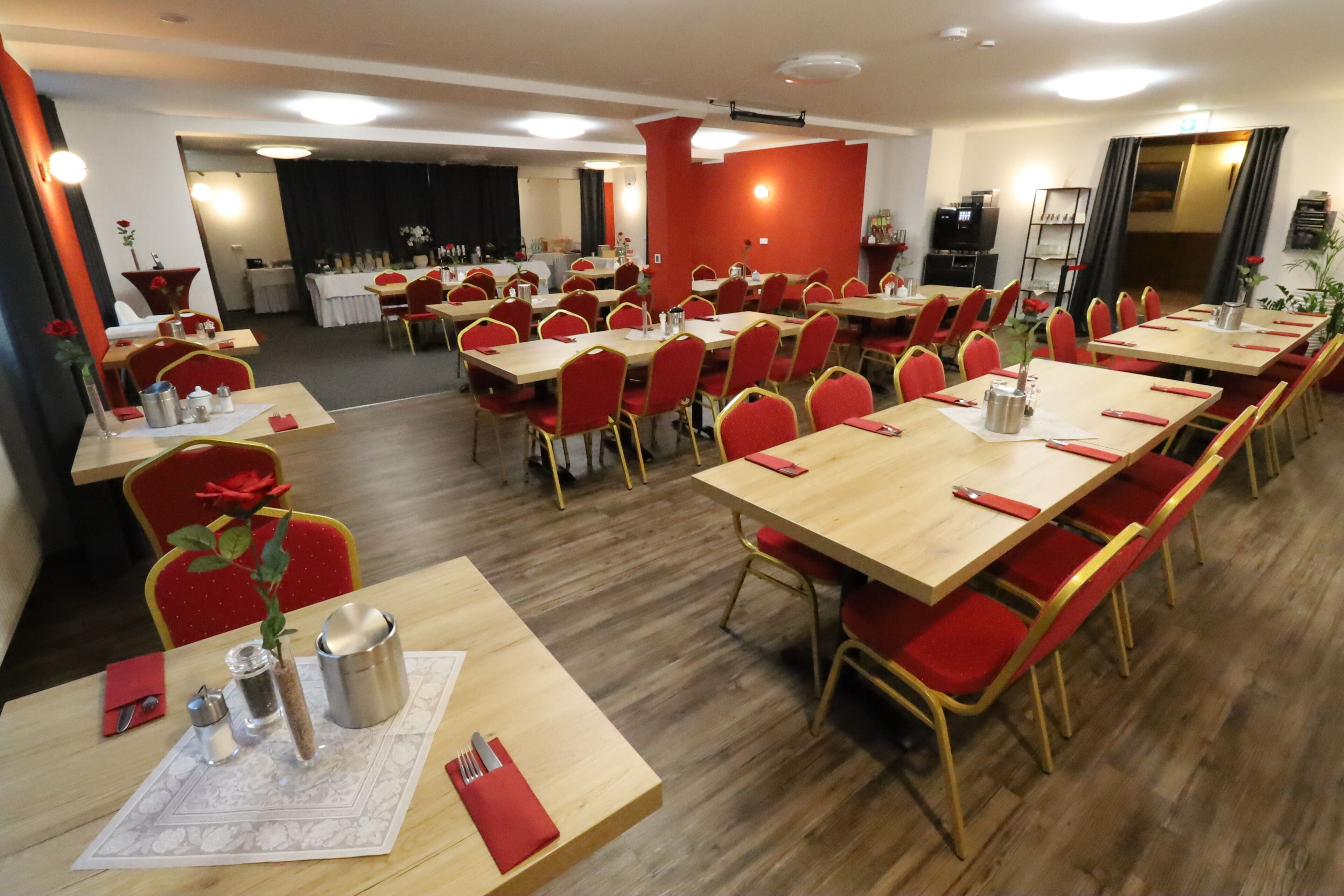 Een restaurantgedeelte in een hotel met meerdere tafels en rode stoelen, compleet met servies en een televisie op de achtergrond.