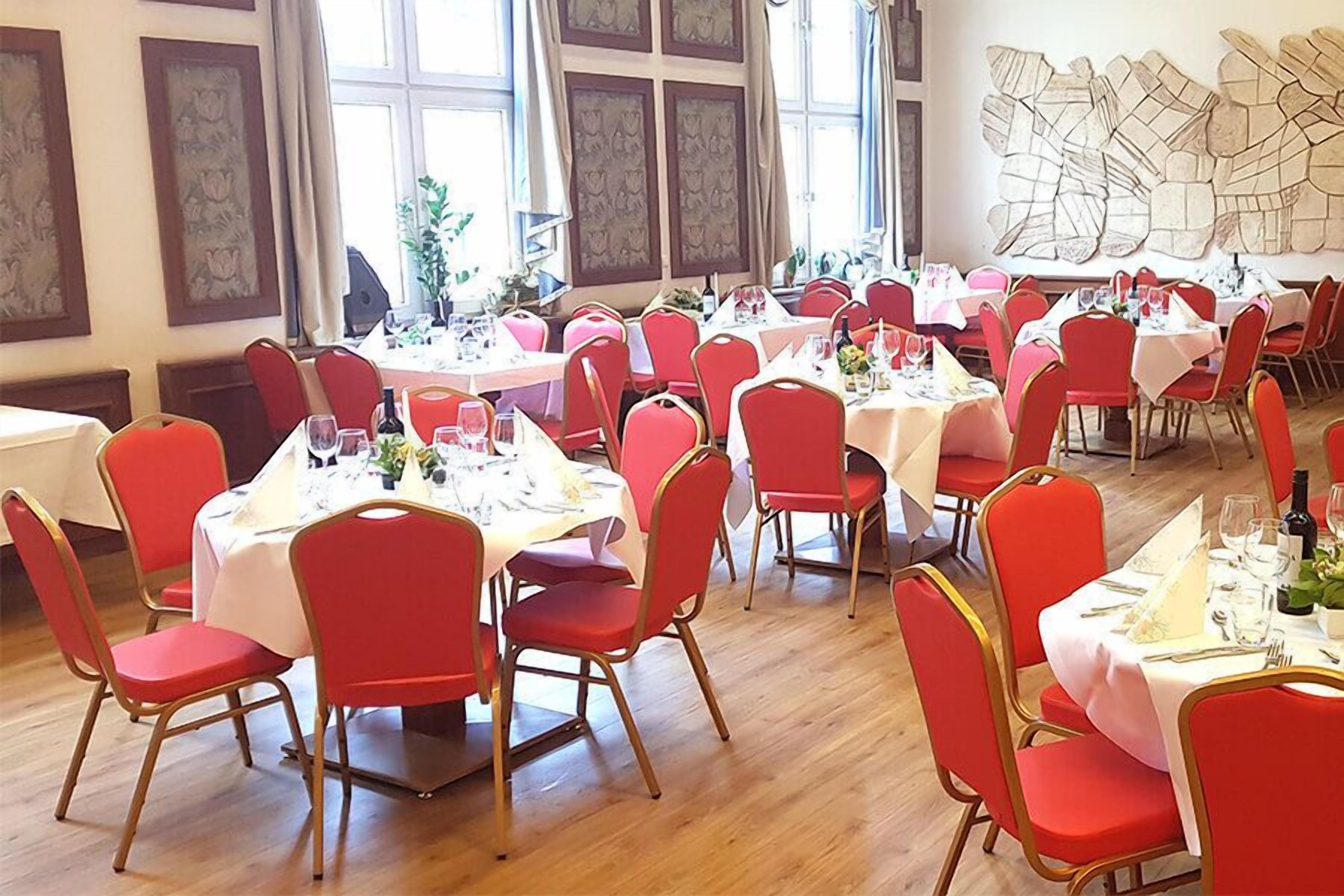 A dining area with multiple round tables, each set with red chairs and white tablecloths.