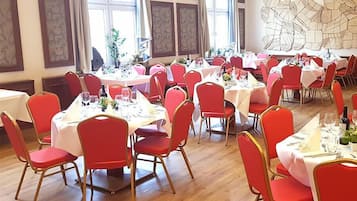 A dining area with multiple round tables, each set with red chairs and white tablecloths.