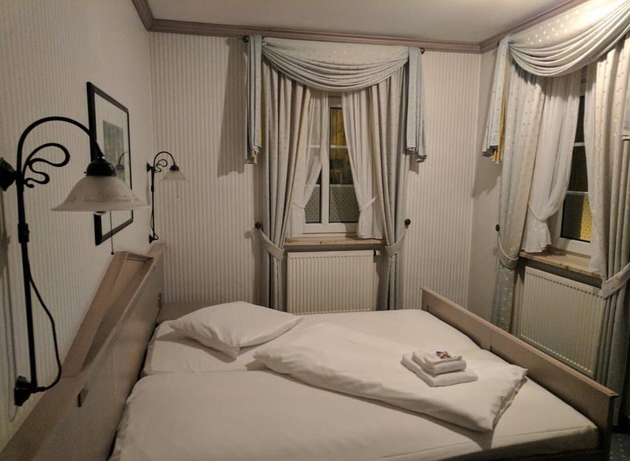 A neatly made bed with white linens, a bedside lamp, and a window with curtains.