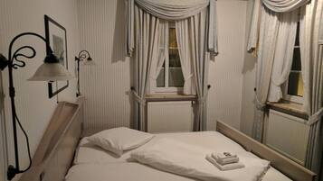 A neatly made bed with white linens, a bedside lamp, and a window with curtains.