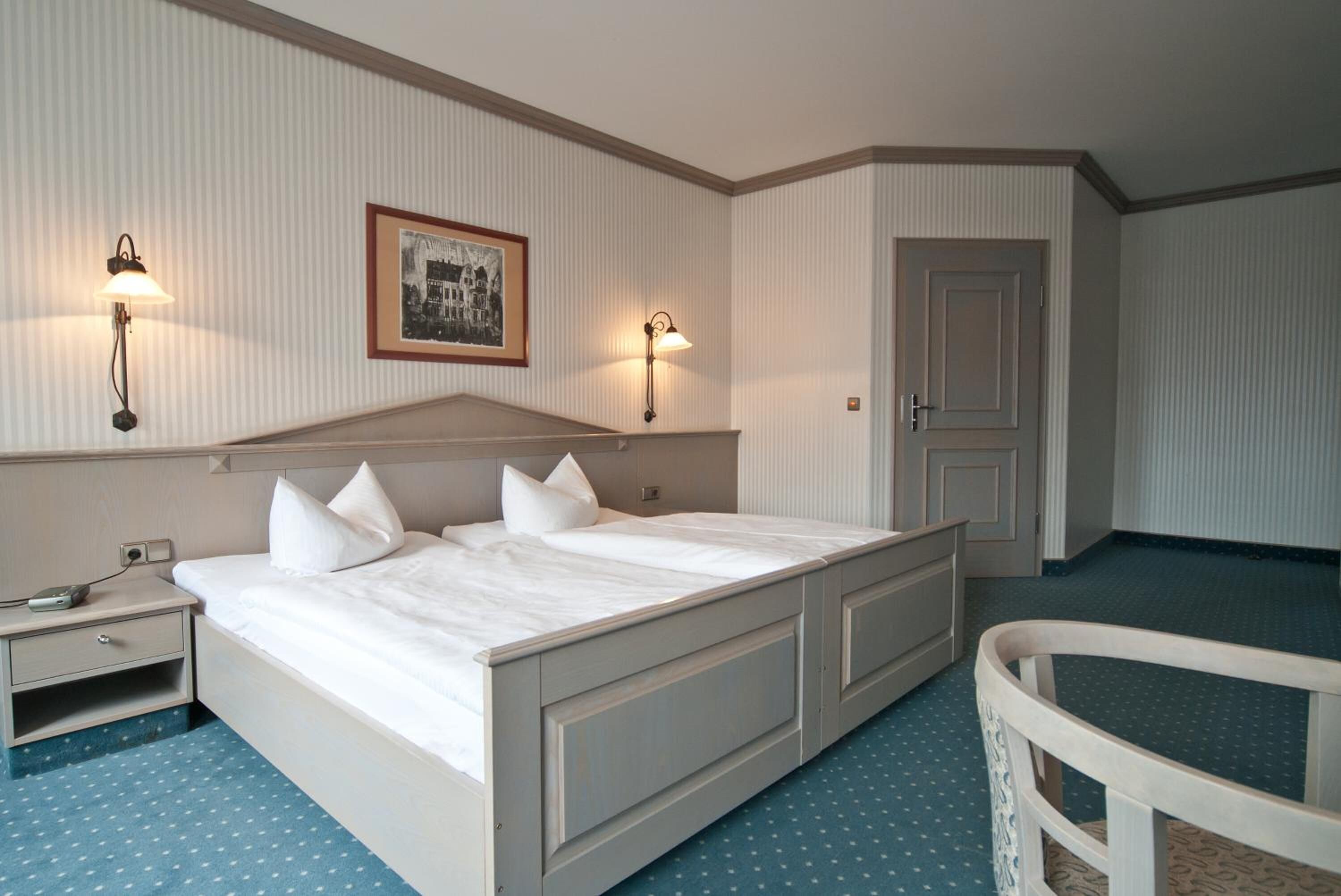 A neatly arranged hotel room with a large bed, bedside tables, wall-mounted lamps, and a framed picture on the wall.