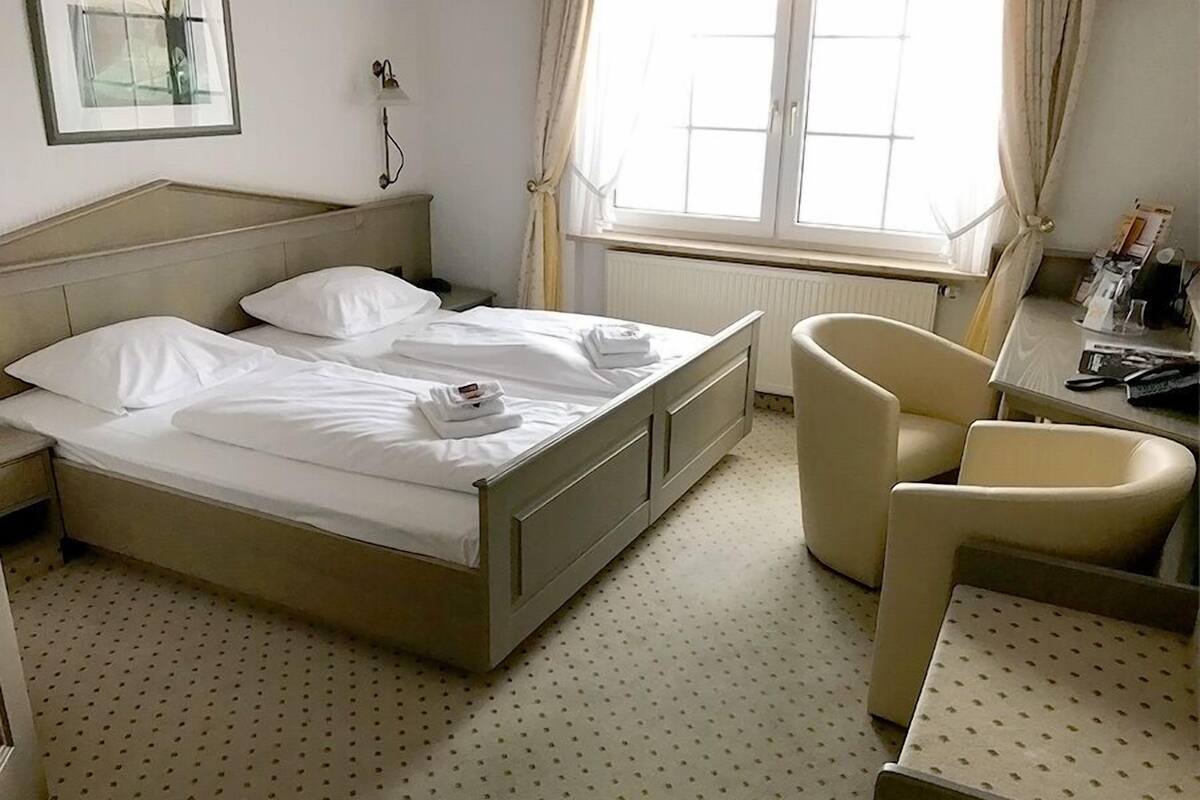 A hotel room with a bed, two chairs, a desk, and a window with curtains.
