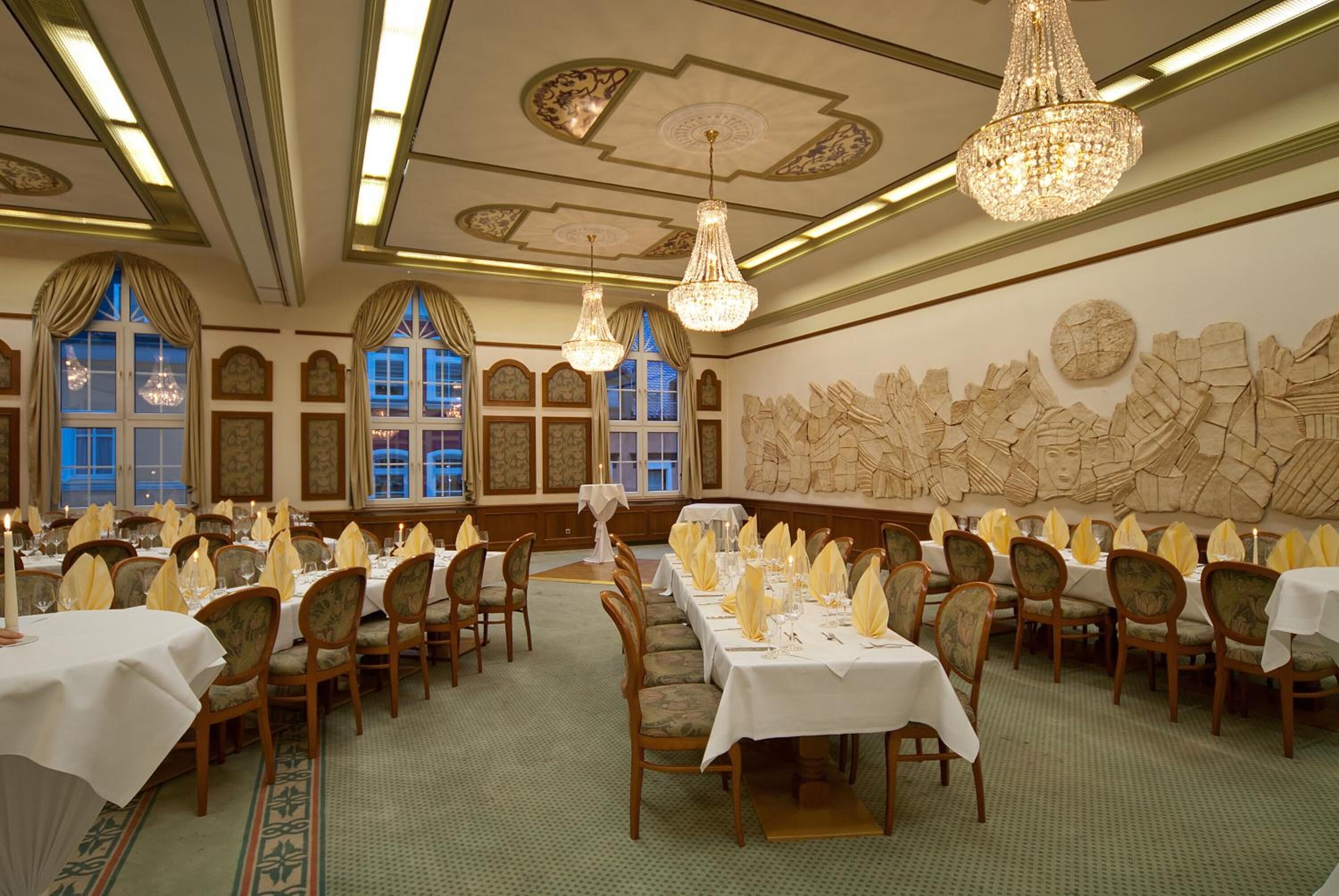 A formal dining room with long tables, chandeliers, and classical wall decorations.