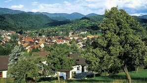 A rural village with houses, a large tree, and mountains in the background. - Hotel garni  Zur Weserei (Kandern)