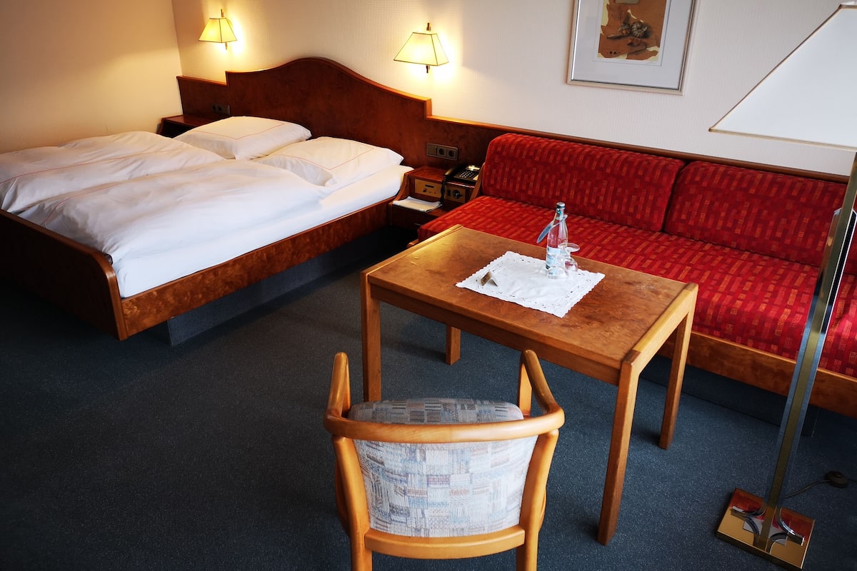Een hotelkamer met een bed, een rode bank, een houten tafel met een fles en een stoel.