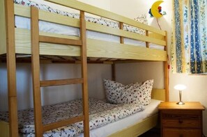 Una cama individual con escalera de madera, una mesita de noche con lámpara y una colcha con estampado floral.