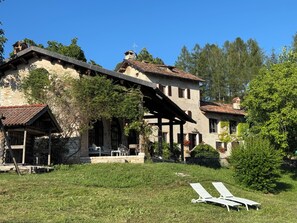 A large stone house with a covered patio and two lounge chairs in the yard.