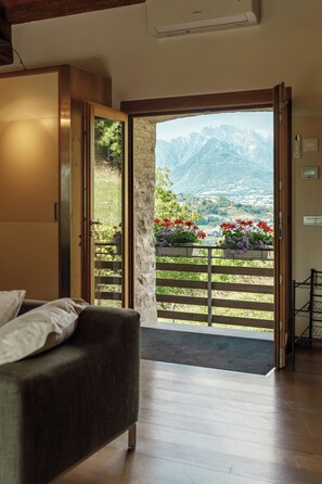 A room with a bed, a wooden wardrobe, and a door leading to a balcony with a mountain view and flower boxes.