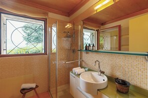 A bathroom with a glass shower door, a sink with a mirror above it, and a window with a view of greenery.